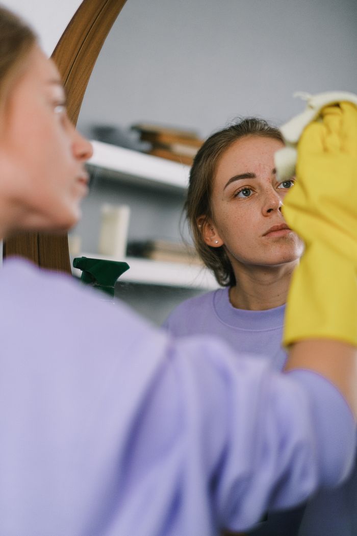 gallery-1 Crop female in purple sweatshirt and latex gloves washing mirror in light apartment in daytime