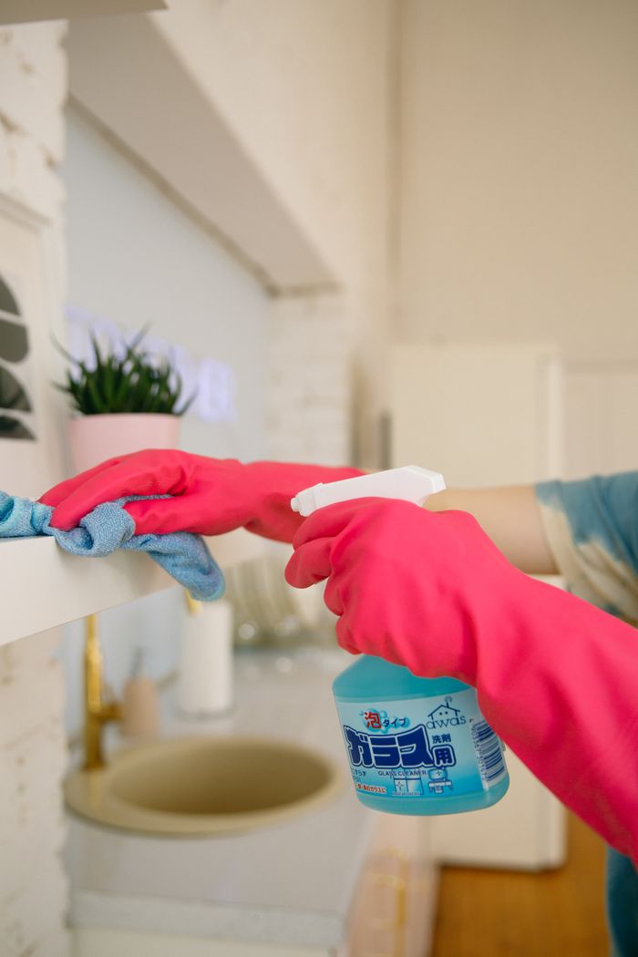 hero-img-01 Person using spray bottle and cloth for cleaning a kitchen shelf, ensuring hygiene and cleanliness.